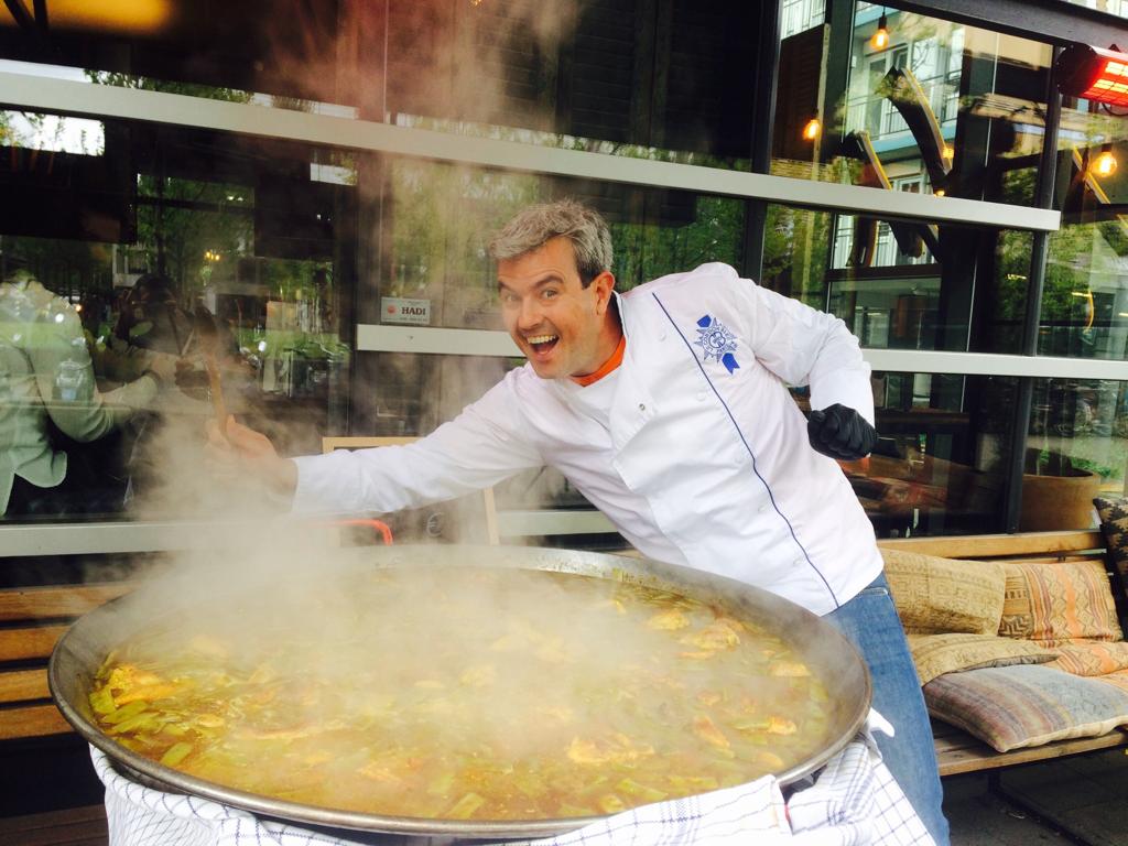Daniel presenteert enthousiast een grote dampende paella